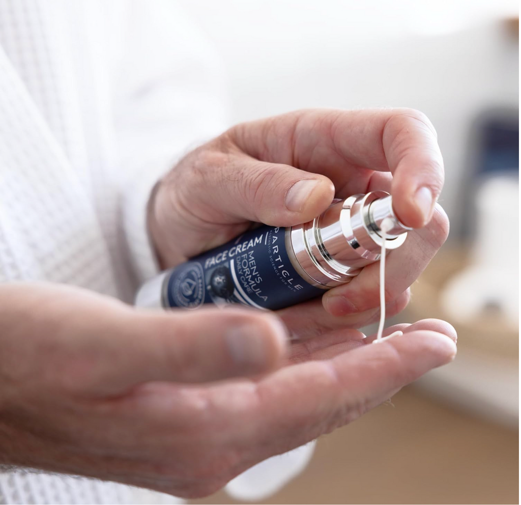 Hand holding a bottle of face cream with visible cream being squeezed out.